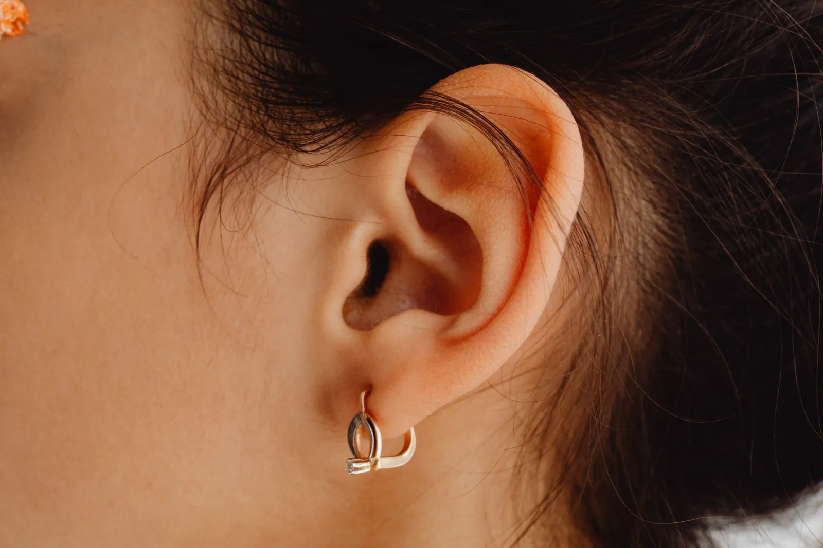 Gros plan sur une oreille de femme portant une petite créole dorée au lobe